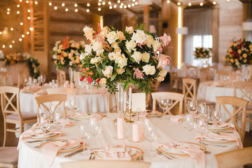 Coziness and style. Modern event design. Table setting at wedding reception. Floral compositions with beautiful flowers and greenery, candles, laying and plates on decorated table.